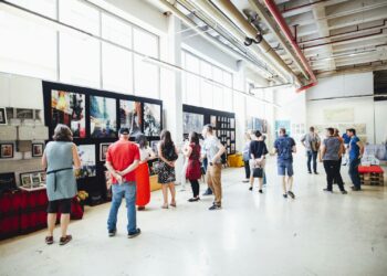 Geniş bir sanat galerisinde sergilenen tablolara bakan kalabalık sanatseverler.