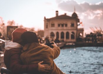 Manzaralı bir sahil kenarında bankta oturup telefonla özçekim yapan bir çift.