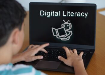 Bilgisayar ekranında Digital Literacy yazısı ve robot illüstrasyonu yer alıyor.