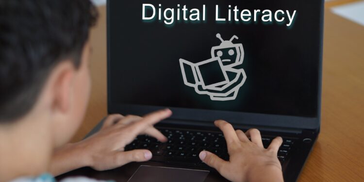 Bilgisayar ekranında Digital Literacy yazısı ve robot illüstrasyonu yer alıyor.