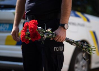 Polis memurunun elinde kurdelelerle bağlanmış kırmızı karanfiller tuttuğu yakın plan çekim