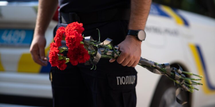Polis memurunun elinde kurdelelerle bağlanmış kırmızı karanfiller tuttuğu yakın plan çekim