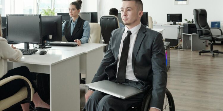 Ofis ortamında tekerlekli sandalyede oturan takım elbise giymiş memur adayı.