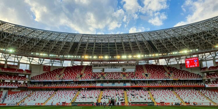 Kırmızı koltuklu boş bir futbol stadyumu ve mavi gökyüzü