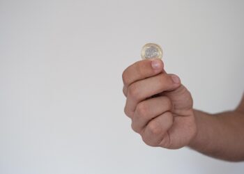Elinde bir euro madeni para tutan erkek eli gri arka plan.
