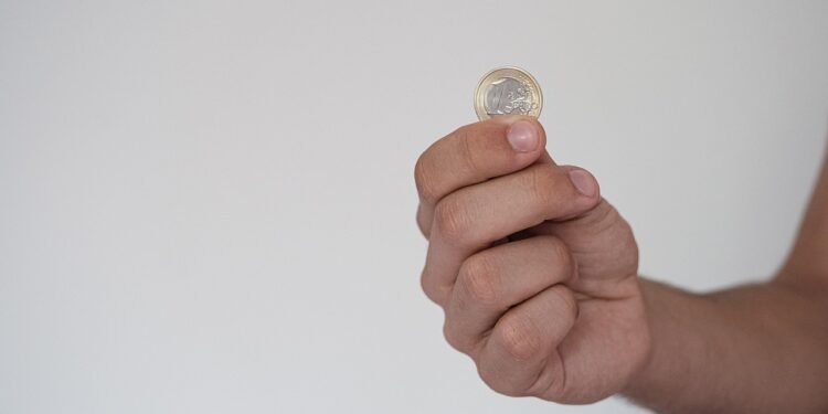 Elinde bir euro madeni para tutan erkek eli gri arka plan.