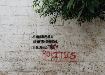 Üzerinde siyaset ve yalan yazan grafitili beyaz tuğla duvar görünümü.