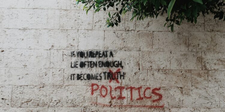 Üzerinde siyaset ve yalan yazan grafitili beyaz tuğla duvar görünümü.