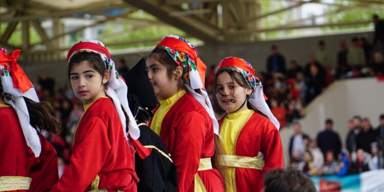 Kırmızı geleneksel kıyafetler giymiş halk oyunları oynayan genç kızlar.