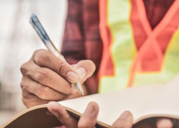 Güvenlik yeleği giymiş bir kişi açık deftere not alıyor.