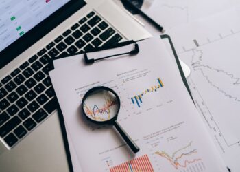 Bilgisayar klavyesi üzerinde büyüteçle incelenen finansal grafikler ve veriler.