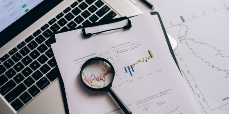 Bilgisayar klavyesi üzerinde büyüteçle incelenen finansal grafikler ve veriler.