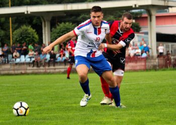 Futbol sahasında top süren ve mücadele eden iki futbolcu.