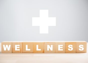 Üzerinde beyaz harflerle 'WELLNESS' yazan ahşap bloklar ve arka planda tıbbi artı simgesi.