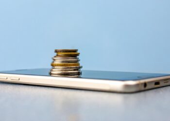 Açık mavi zemin üzerinde bir akıllı telefon ve üzerinde yükselen madeni paralar.