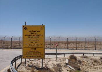 Çöl benzeri bir arazide Batı Şeria sınırındaki güvenlik çiti ve uyarı levhası.