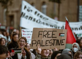 Kalabalık protestoda 'Free Palestine' yazılı döviz taşıyan gençler.