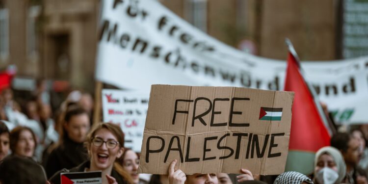 Kalabalık protestoda 'Free Palestine' yazılı döviz taşıyan gençler.