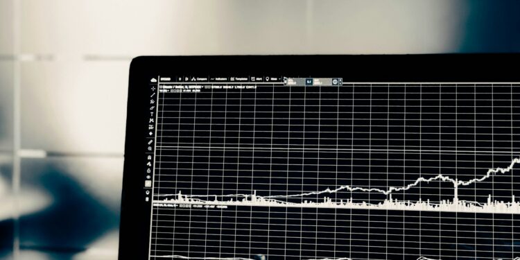 Bilgisayar ekranında beyaz renkli grafik çizgileri ve finansal veriler bulunuyor.
