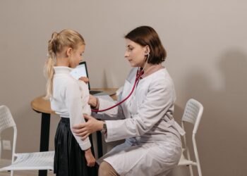 Bir çocuk doktoru muayenehanesinde küçük kız hastayı stetoskopla muayene ediyor.