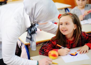 Sınıfta öğretmen bir kız öğrencinin başını okşayarak onunla ilgileniyor.